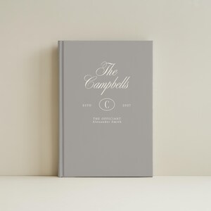 May include: A gray hardcover book featuring white text that reads The Campbells, ESTD 2027, with a central oval containing the letter C, and the text THE OFFICIANT Alexander Smith printed below the oval in a clean, centered layout.