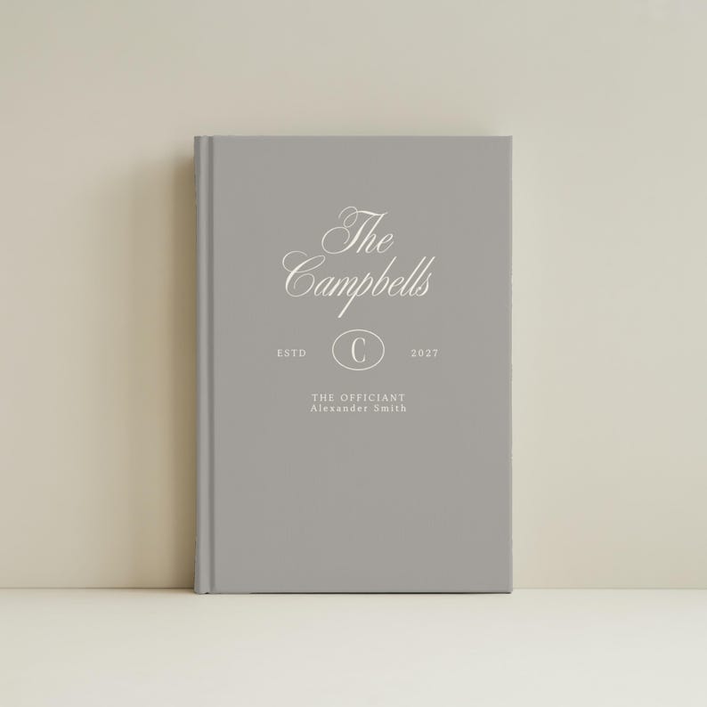 May include: A gray hardcover book featuring white text that reads The Campbells, ESTD 2027, with a central oval containing the letter C, and the text THE OFFICIANT Alexander Smith printed below the oval in a clean, centered layout.