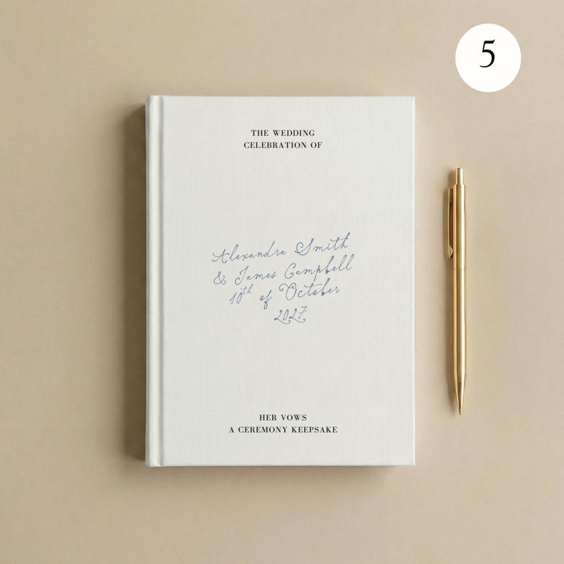 May include: A white hardback book with the text THE WEDDING CELEBRATION OF, Alexandra Smith & James Campbell 10th of October 2027, HER VOWS A CEREMONY KEEPSAKE printed on the cover, accompanied by a gold-coloured metal pen placed to the right.