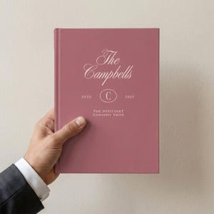 May include: A dusty rose hardcover book featuring white text that reads The Campbells, ESTD 2027, a central letter C inside an oval, and the text THE OFFICIANT Alexander Smith printed on the front cover in a clean, centered layout.