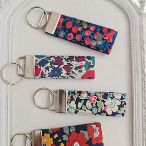 Könnte beinhalten: Vier Schlüsselanhänger aus Stoff mit Blumenmustern in Rot, Blau, Gelb und Weiß. Jeder Schlüsselanhänger hat einen silberfarbenen Metallverschluss und -ring. Die Schlüsselanhänger sind rechteckig und scheinen aus Baumwollstoff zu sein.