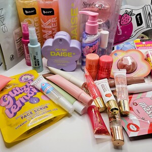 May include: A collection of beauty and skincare products including b.pure shimmer gels, a Vivitar Simply Beautiful set, Oh So Daise fragrance mist, various lip glosses, lipsticks, face masks, and a Gitz Lemon face scrub packet with hyaluronic acid.