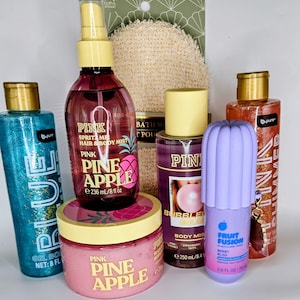May include: A collection of bath and body products including a blue glitter gel body wash, a Pink Pineapple hair and body mist, a Pink Pineapple body scrub, a Bubble Beach body mist, a purple Fruit Fusion perfume mist, and a shimmer body wash.