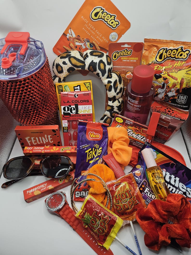 May include: A collection of items including a red studded tumbler, a leopard print headband, Cheetos snacks, Takis, Hot Pops, Skittles, L.A. Colors nail tips, a Pink body mist, sunglasses, a red watch, orange scrunchies, and various beauty products.