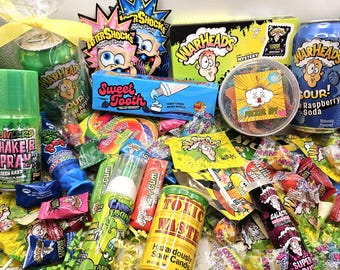 May include: A collection of assorted sour sweets and sodas including Warheads, Toxic Waste, and Sweet Tooth products. The assortment features various colourful wrappers, spray sweets, popping candy packets, and two cans of flavoured soda.