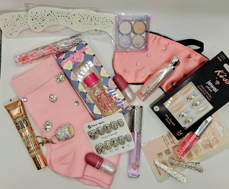 May include: A collection of beauty and fashion items including pink ribbed socks with rhinestones, a Kiss Jewel press-on nail set, a pink sleep mask with pearls, various lip glosses, a primer bottle, a small eyeshadow palette, and hair clips.