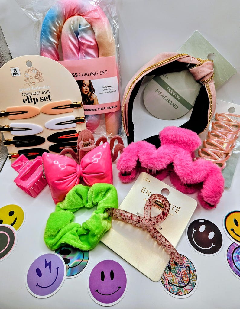 May include: A collection of hair accessories including a tie-dye curling set, a pink headband with gold chain detail, a bright pink bow clip, a fuzzy pink claw clip, a neon green scrunchie, a glittery hair clip, and various smiley face stickers.