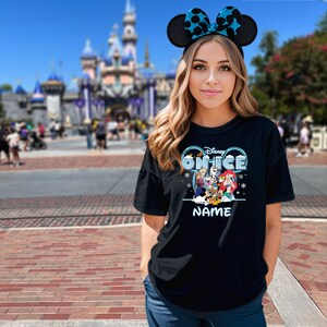 A young woman wearing a Disney-themed t-shirt and Mickey Mouse ears stands in front of a Disney castle.