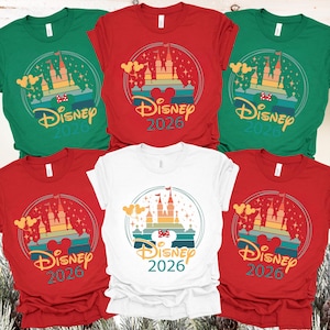 May include: A selection of red, green, and white t-shirts. Each shirt displays a castle design with the text "Disney 2026". The design incorporates Mickey Mouse ears and a rainbow-coloured background.