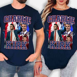May include: Navy blue t-shirts featuring a graphic of a man with the text "CHARLIE KIRK" in red and white. The design includes images of the man against a backdrop of the American flag.