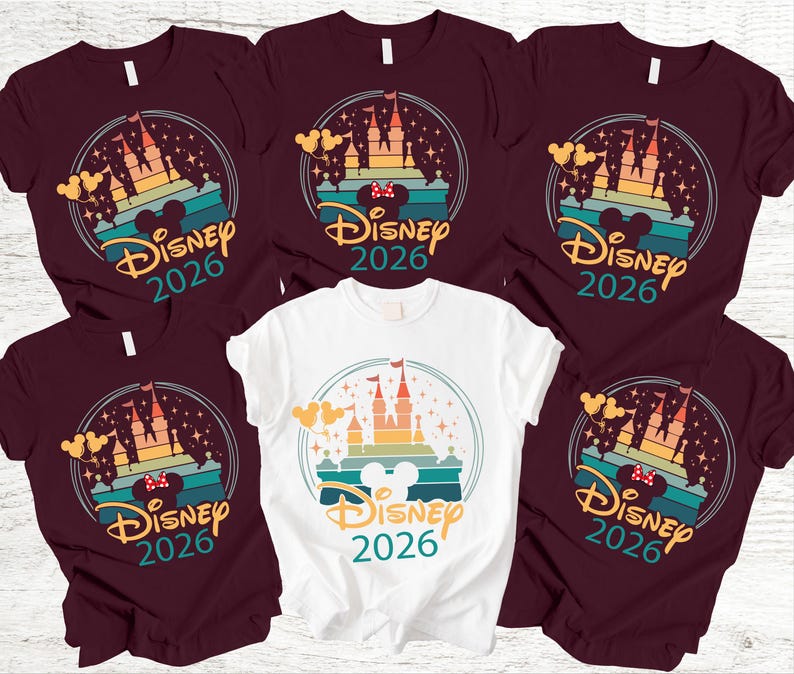 May include: Several maroon and white t-shirts with a colourful graphic design. The design features a castle, Mickey Mouse ears, and the text "Disney 2026" within a circular frame. The shirts are short-sleeved.