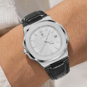 May include: A silver-toned wristwatch with a textured face and a black leather band is shown. The watch has a date display and a small dial on the side. The watch is secured on a wrist.