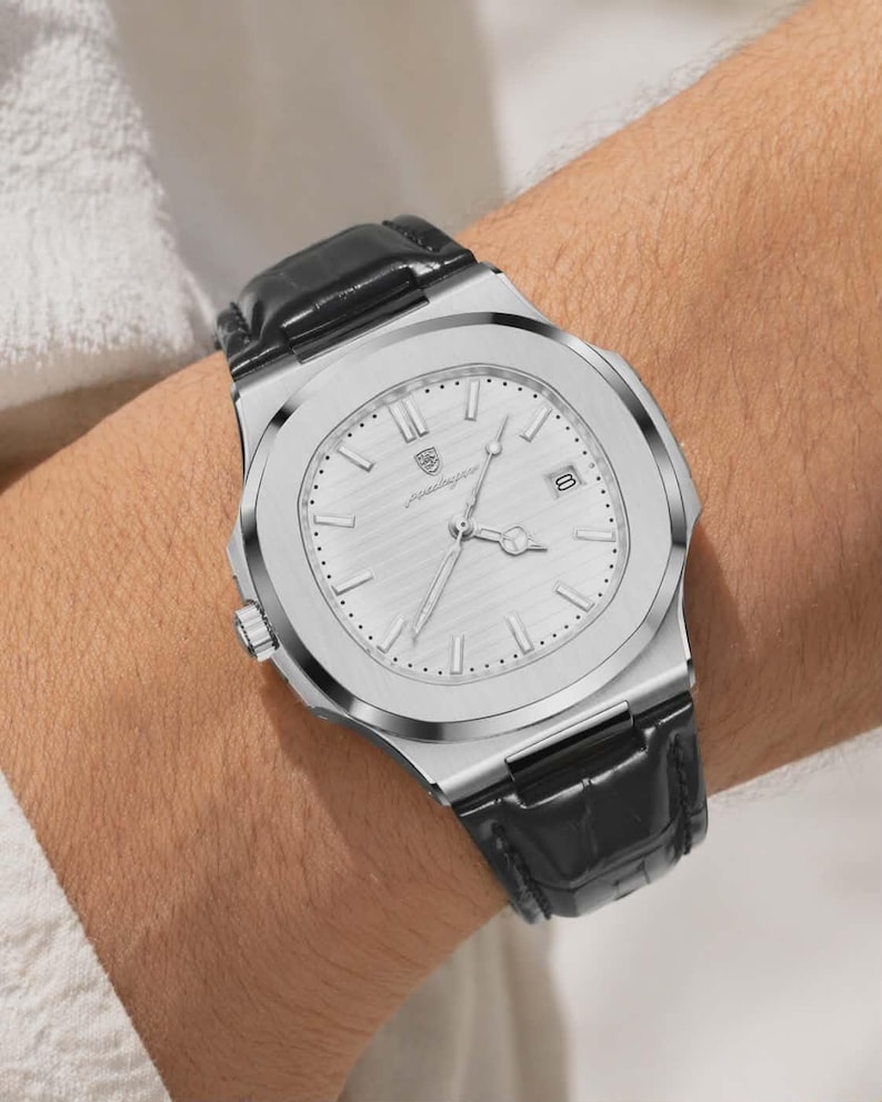 May include: A silver-toned wristwatch with a textured face and a black leather band is shown. The watch has a date display and a small dial on the side. The watch is secured on a wrist.