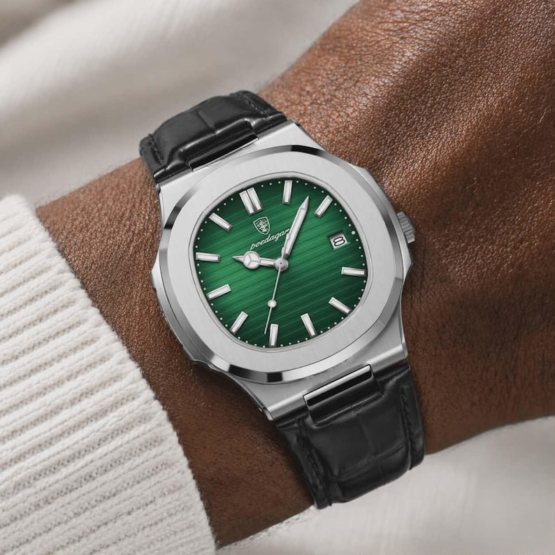 May include: A stainless steel wristwatch with a green dial and black leather band. The watch features a date display and luminous hands. The watch is shown on a wrist, with a white sweater in the background.