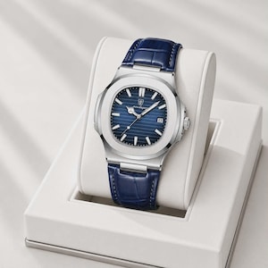 May include: A silver-toned wristwatch with a blue dial and a blue leather strap. The watch has a rectangular face with a date display and is presented on a white display stand. The watch band is approximately 8 inches long.