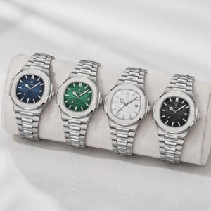 May include: Four stainless steel watches with blue, green, white, and black faces. Each watch has a silver strap and a round face with hour markers and hands. The watches are displayed on a white, cylindrical cushion.