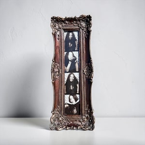 May include: A tall, rectangular picture frame with an ornate, dark bronze-colored finish featuring intricate floral and scrollwork carvings. The frame holds a vertical strip of four black and white photographs showing a person in various poses.