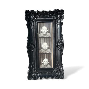 May include: A black, ornate picture frame with three vertical photo booth-style images. Each image features a black and white portrait of a person with a smiling expression. The frame has decorative floral and scroll details.