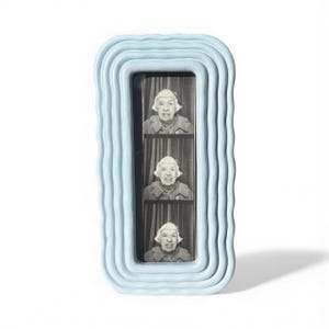 Puede incluir: Un marco de fotos azul claro con bordes ondulados que contiene tres fotos en blanco y negro de la misma mujer. El marco tiene una abertura rectangular y un diseño texturizado en capas.