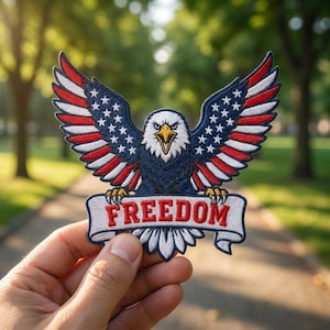 May include: Embroidered patch featuring an American bald eagle with outstretched wings. The wings display the stars and stripes of the American flag. The eagle holds a banner with the word "FREEDOM" in red letters.