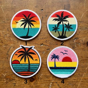May include: Four round embroidered patches with a tropical sunset theme. Each patch features a palm tree silhouette against a colorful sky, with variations in the number of trees and sunset colors. The patches have a white border.