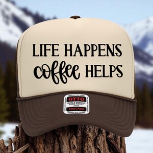 Puede incluir: Gorra de camionero marrón y beige con el texto negro "LIFE HAPPENS coffee HELPS". La gorra tiene una visera marrón y un cierre a presión. Fabricada en tejido de espuma.
