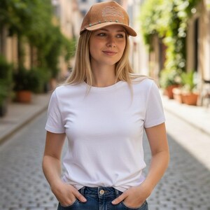 K&ouml;nnte beinhalten: Braune Trucker-M&uuml;tze mit Bergmotiv und t&uuml;rkisfarbenen Perlen. Die M&uuml;tze wird mit einem wei&szlig;en T-Shirt und einer blauen Jeans getragen. Das Bild wird im Freien auf einer Kopfsteinpflasterstra&szlig;e aufgenommen.
