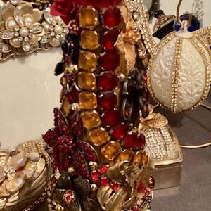 May include: A decorative bottle stopper made of glass, rhinestones, and metal. The stopper is shaped like a Christmas tree and is decorated with red, gold, and clear rhinestones. The stopper is topped with a clear crystal.