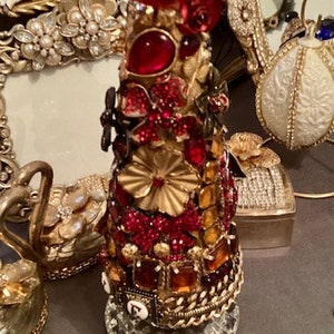 May include: A decorative bottle stopper with a crystal top and a base covered in red, gold, and orange jewels.