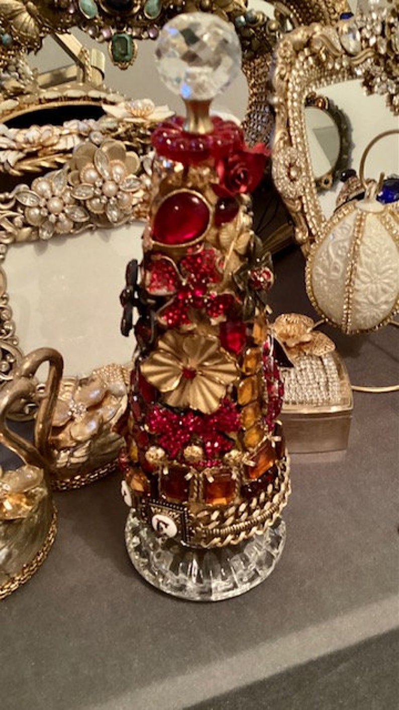 May include: A decorative bottle stopper with a crystal top and a base covered in red, gold, and orange jewels.