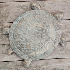 May include: A decorative turtle sculpture with a textured, light blue and beige finish. The turtle has a detailed shell pattern and four protruding flipper-like legs and a head. The sculpture is made of a durable material.