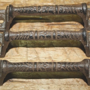 May include: Three rustic, cast iron handles with a distressed, brown finish. Each handle features a textured grip and decorative end plates with pre-drilled holes for mounting. Ideal for cabinet doors or drawers.