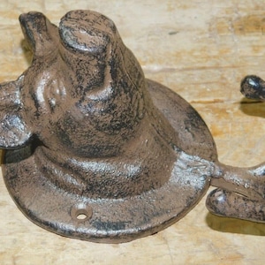 May include: A cast iron wall hook in the shape of a dog's head. The hook is brown with black accents and a circular base. The dog's head is detailed with visible ears and snout. The hook curves downward, providing a place to hang items.