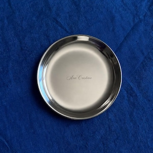 May include: A circular, polished silver-toned metal tray with a smooth, reflective surface. The center of the tray features the name Ana Cristina engraved in a delicate, cursive script font, centered horizontally within the round basin.