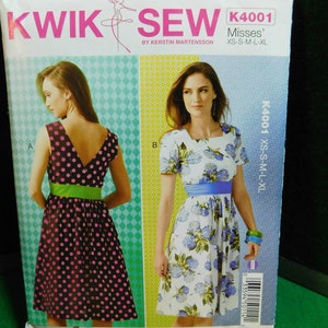 Könnte beinhalten: Ein Schnittmuster für zwei Kleider, eines mit Punkten und einer grünen Schärpe, das andere mit Blumenmuster und einer blauen Schärpe. Das Schnittmuster heißt "Kwik Sew" und ist für Damen in den Größen XS-S-M-L-XL.