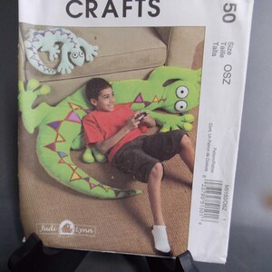 May include: A sewing pattern for a green lizard-shaped pillow. The pattern is from McCall's Crafts and is for size OSZ. The pattern includes instructions for making a pillow that looks like a lizard.