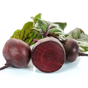 May include: Three fresh beets with vibrant green leaves. One beet is cut in half, revealing a deep red interior. The beets are a dark reddish-purple color, with long, thin root stems. The leaves have a mix of green and purple hues.