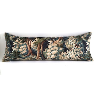 May include: A long, rectangular decorative pillow with a forest scene design. The pillow features a dark blue background with trees in shades of brown, green, and cream. The pillow is designed to be used as a decorative accent on a bed or sofa.