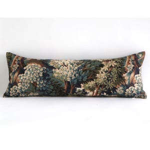 May include: A long, rectangular cushion with a forest scene design. The cushion features a tapestry-like pattern with trees in shades of green, brown, and blue. It is designed for use on a bed or sofa.