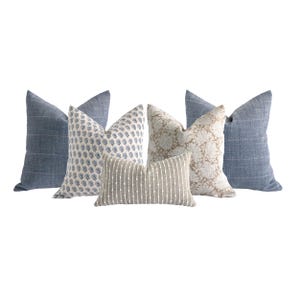 May include: A collection of five decorative throw pillows featuring two blue pillows with white horizontal lines, one blue and white floral print pillow, one beige textured pillow with a floral pattern, and one small rectangular beige pillow with white dots.
