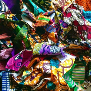 May include: A pile of colorful fabric scraps in various patterns and colors, including purple, orange, green, and yellow. The fabric pieces are cut into irregular shapes and sizes, creating a textured and layered appearance. The image showcases a variety of African wax print textiles.
