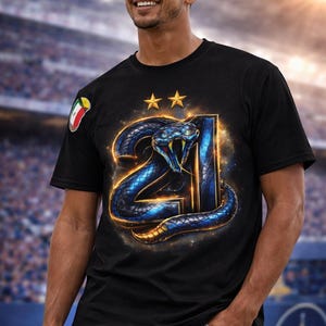 Könnte beinhalten: Schwarzes T-Shirt mit einem blau-goldenen Schlangenmuster, das sich um die Zahl 21 windet, mit zwei goldenen Sternen darüber. Auf dem linken Ärmel befindet sich ein farbenfrohes Emblem. Das Design hat einen Leuchteffekt.