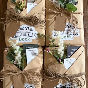 May include: Four wrapped gifts with the text "Blind Date with the Book" on each. The gifts are wrapped in brown paper, tied with twine, and decorated with faux flowers and tags. Each gift contains a card that says "What's Included".