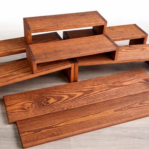 Puede incluir: Expositores de madera en varios tamaños y configuraciones. Los expositores están teñidos de un color marrón cálido, mostrando la veta natural de la madera. El conjunto incluye plataformas rectangulares y soportes escalonados.