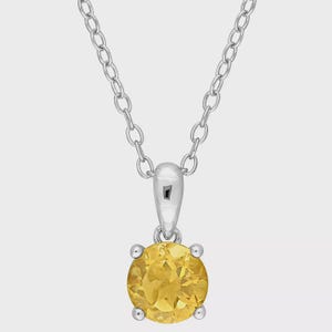 May include: A silver necklace with a round, yellow gemstone pendant. The gemstone is held in place by four small prongs. The chain is a simple link style.