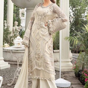 May include: An ivory-colored, embellished formal dress with long sleeves and wide-leg pants. The dress features intricate beadwork and lace details. The sleeves have a bell shape. The outfit is suitable for special occasions.