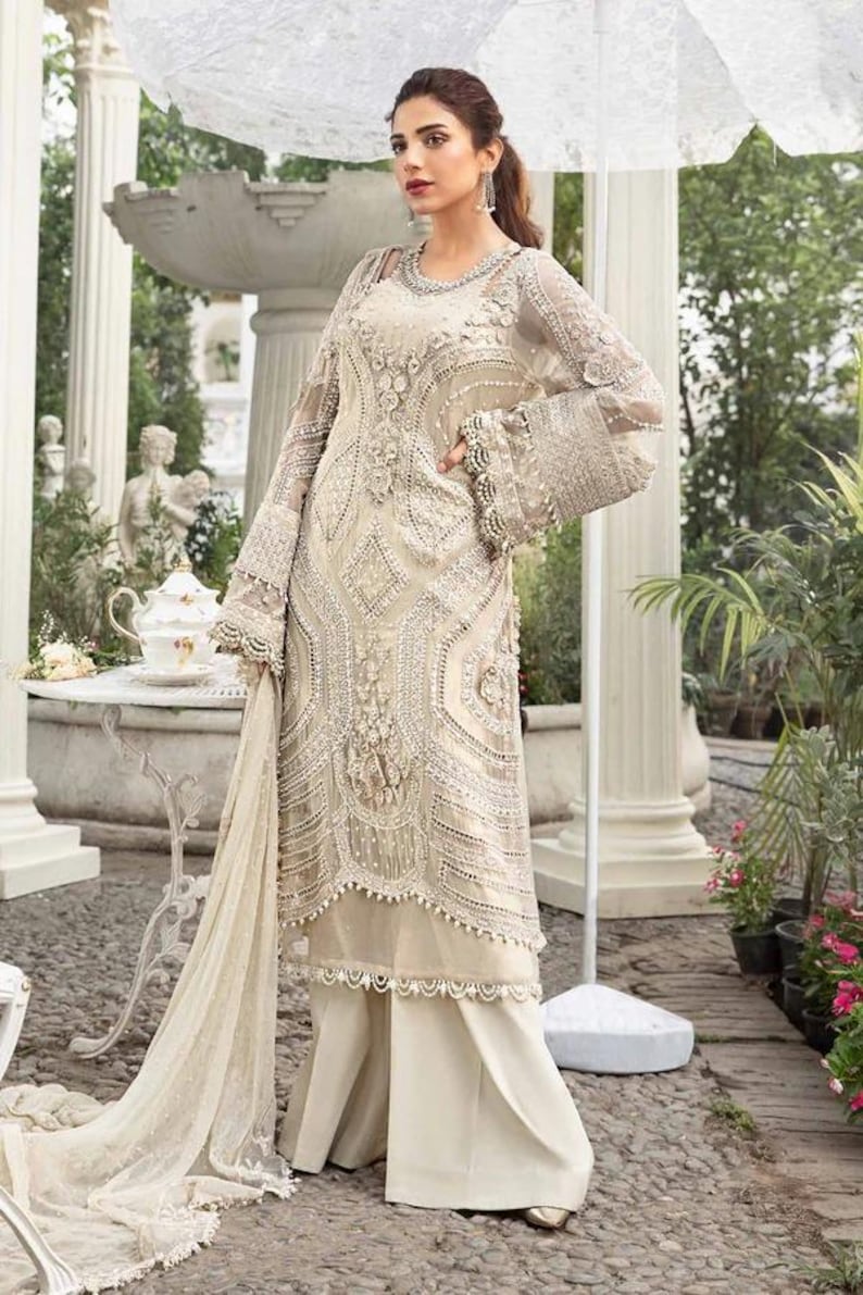 May include: An ivory-colored, embellished formal dress with long sleeves and wide-leg pants. The dress features intricate beadwork and lace details. The sleeves have a bell shape. The outfit is suitable for special occasions.