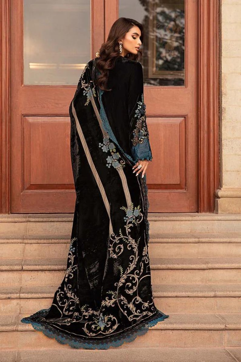 May include: A long, black velvet garment with intricate floral embroidery in teal and cream. The garment features a flowing design with a detailed border and accents on the sleeves. The elegant piece is suitable for special occasions.