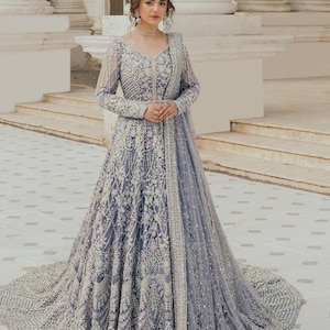 May include: A long, light blue formal gown with intricate silver embroidery and beadwork. The dress features long sleeves, a V-neck, and a flowing skirt with a train. A matching shawl is draped over the shoulders.