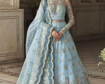 May include: A light blue formal gown with intricate silver embroidery and embellishments. The gown features long sleeves, a sheer bodice, and a flowing skirt. A matching sheer shawl with a detailed border completes the ensemble. The dress is suitable for special occasions.